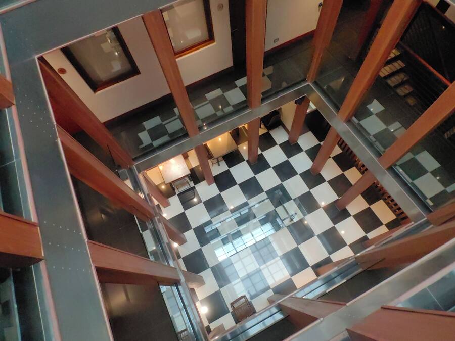 Vista aérea del interior de un edificio con suelo de estampado de cuadros, elementos estructurales de madera y barandillas de cristal.