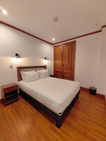 Un dormitorio con una cama grande, un armario de madera, lámparas de noche y una mesita auxiliar.
