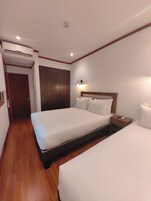 A hotel room with a large bed, a bedside table, a wardrobe, and an air conditioning unit.