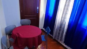 Een kamer met een houten deur, een ronde tafel met een rode tafelkleed, en blauwe stoelen.