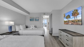 A modern hotel room with two beds, a wooden dresser, a painting of palm trees, and a view of the beach. - Boardwalk Resort: Ocean Breeze Retreat (Myrtle Beach)