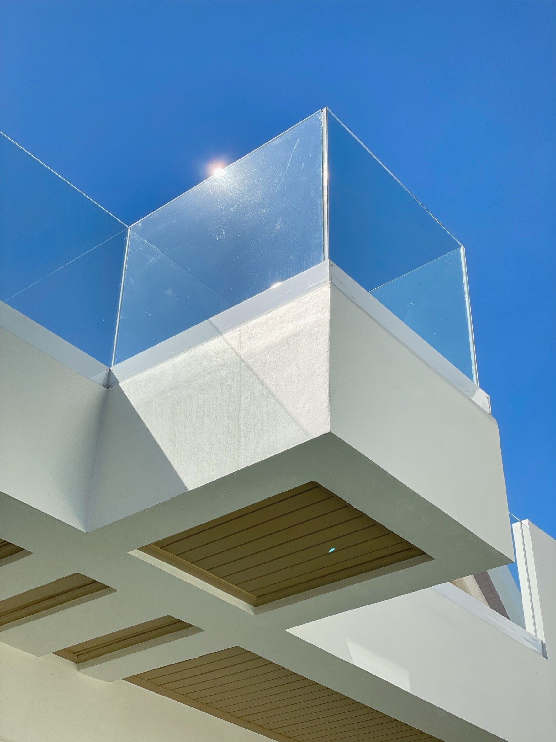 A modern building with a glass enclosure on the upper level, wooden beams on the lower level, and a clear blue sky in the background.