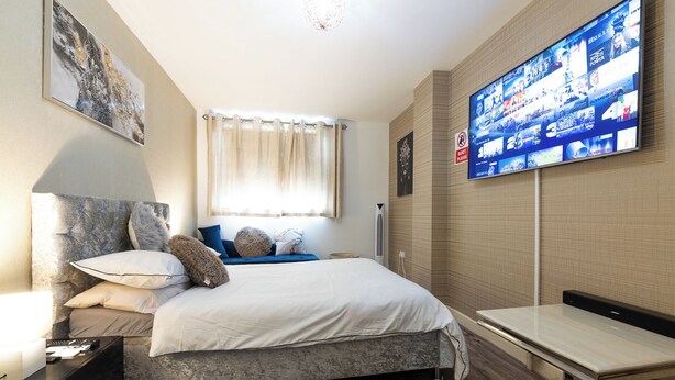 Una habitación de hotel moderna con una cama grande, un televisor montado en la pared y una mesita de noche.