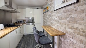 Una cocina moderna con armarios blancos, una campana de acero inoxidable, un microondas y un tostador. Hay una encimera de madera y un banco con tapa de madera.