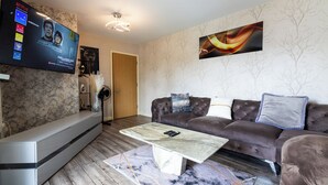 Una sala de estar moderna con un televisor de pantalla plana montado en la pared, un sofá de cuero marrón, una mesa de centro blanca y un suelo con estampado de mármol.