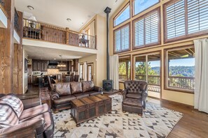 A spacious living area with leather sofas, a coffee table, and large windows offering a view of the outdoors. - Zion Views- East Rim Lodge+ Resort Access (Orderville)