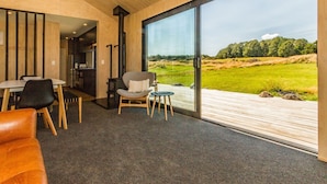Un interior moderno con un gran ventanal que da a una vista exterior, un comedor con mesa y sillas, y una zona de estar acogedora con sofá y sillón.
