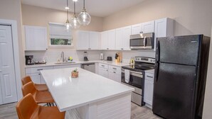 A modern kitchen with white cabinetry, a black refrigerator, and a central island with chairs. - Beautiful Fenced 3BR 2BA Near Exciting Downtown (San Antonio)