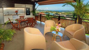 A covered outdoor dining area with wicker furniture, a glass table, and a view of the landscape. - F3 Hibiscus - vue mer - Piscine Chauffée - 9 min de la mer (La Trinité)