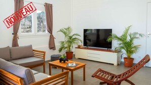 A living room with a sofa, chairs, a coffee table, a TV, and two potted plants. - F3 Hibiscus - vue mer - Piscine Chauffée - 9 min de la mer (La Trinité)