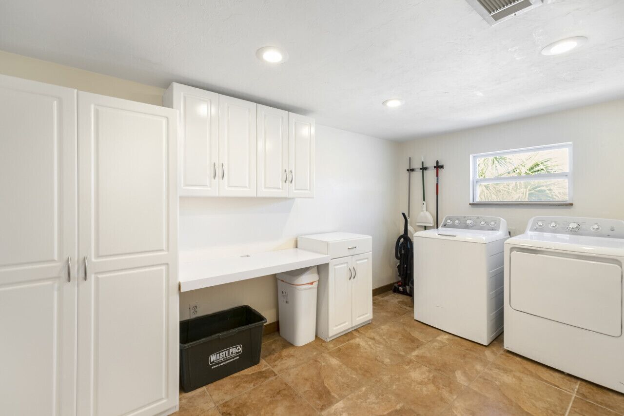 A laundry room with white cabinets, a washing machine, a dryer, and a trash bin.