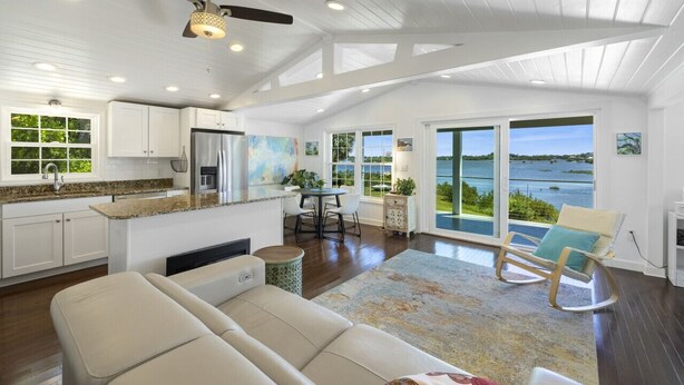 A spacious living area with a large window offering a view of the water, a ceiling fan, and a dining area with a view.