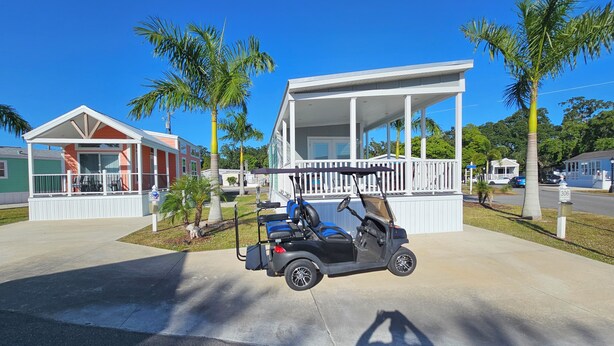 Um carrinho de golfe estacionado em frente a uma casa com varanda e quintal cercado.