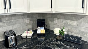 A kitchen with white cabinets, a marble countertop, a coffee maker, a toaster, a Hello sign, and a vase with flowers. - Cozy Modern Utica Retreat 2BD • Private Home • Near Hospital, Downtown & Dining (Utica)