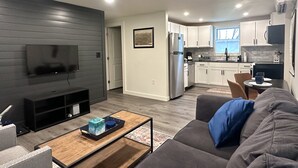A modern living room with a flat-screen TV, a gray sofa, and a wooden coffee table. - Cozy Modern Utica Retreat 2BD • Private Home • Near Hospital, Downtown & Dining (Utica)