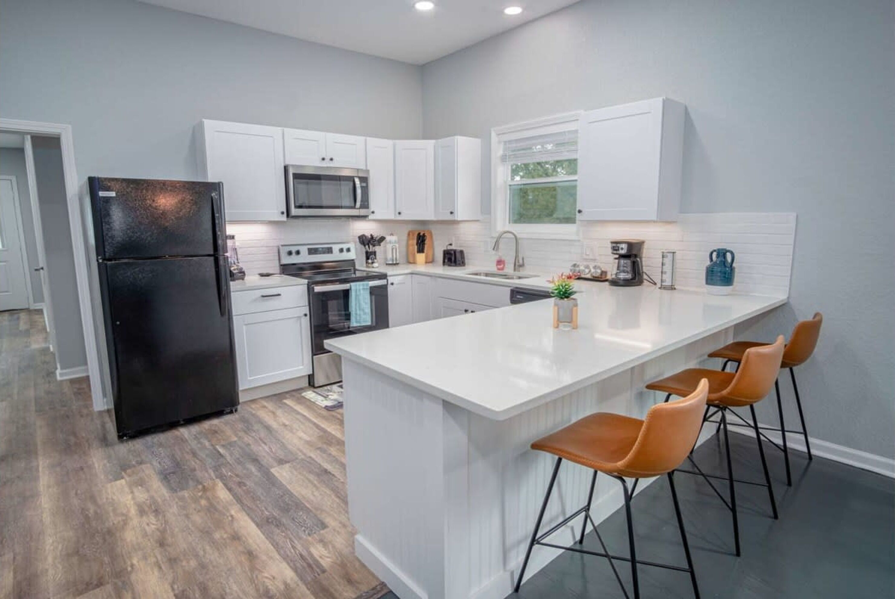 A modern kitchen with white cabinetry, a black refrigerator, a microwave, and a large island with bar stools.