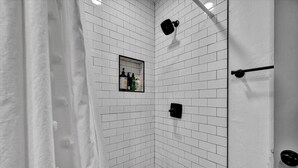 A corner shower with white tiled walls, a small shelf with toiletries, and a towel rack. - OSU Weekend Retreat - Steps to Campus (Stillwater)