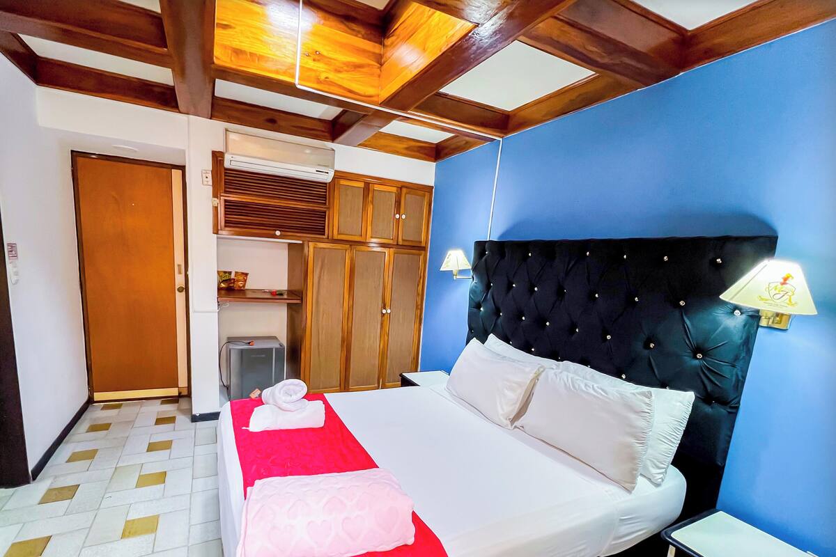 A simple hotel room with a bed, a nightstand, a wardrobe, and a small kitchenette.
