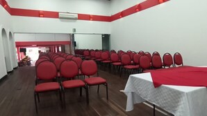 A conference room with rows of red chairs, a white table with a red tablecloth, and a wooden floor. - Hotel Mariscal Robledo Cartago  (Cartago)