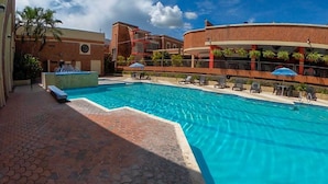 A swimming pool with lounge chairs and umbrellas, surrounded by buildings with balconies and palm trees. - Hotel Mariscal Robledo Cartago  (Cartago)