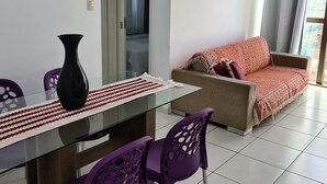 A modern living room with a glass dining table, purple chairs, a beige sofa, and a black vase. - Grande Apartamento Beira-Mar (Maceió)