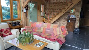 A cozy living room with a wooden staircase, a white sofa, a wooden coffee table, and a green plant.