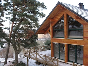 Una cabaña de madera con balcón y ventanas amplias, rodeada de árboles y un paisaje nevado.