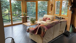 A cozy cabin interior with a sofa, a table, and a view of a wooden deck and trees.