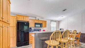A kitchen with wooden cabinets, a black refrigerator, a microwave, and a bar area with wooden stools. - 7 Mi to Crystal River: Home w/ Yard & Fire Pit! (Dunnellon)