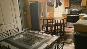 Ett kök med ett matbord, stolar, ett kylskåp, en spis och upphängda kastruller.
