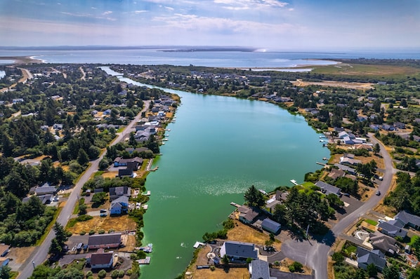 An aerial view of a residential area with houses along a river, roads, and a distant coastline.