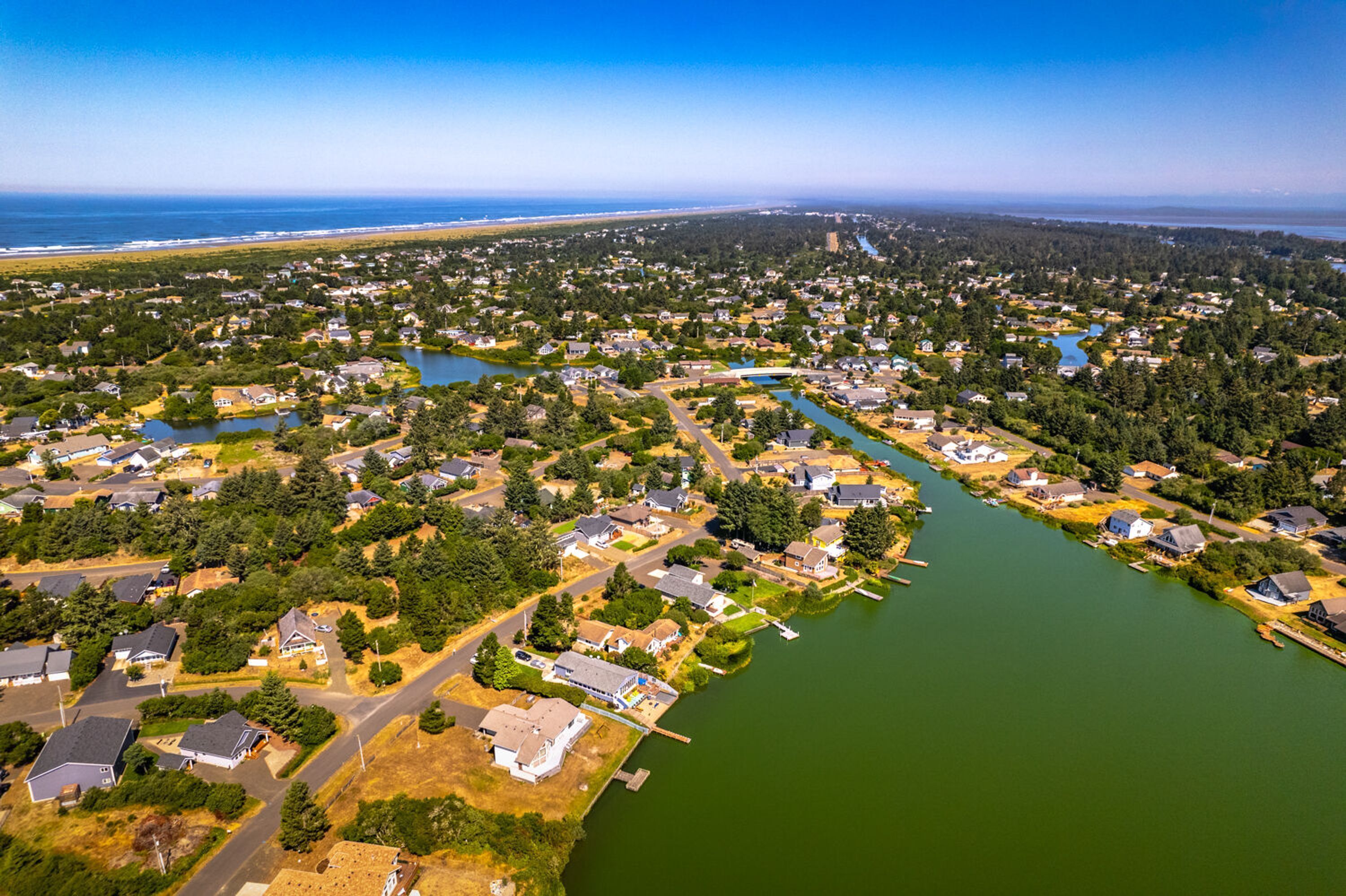 Vista aérea de una zona residencial con casas, un río y una playa al fondo.