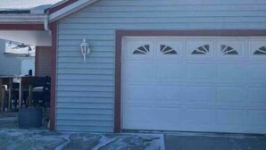A single-story building with a garage door, a small porch area, and a visible trash bin.