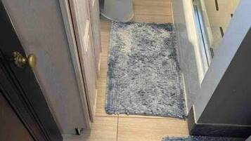 Een kleine badkamer met toilet, vloerkleed en een deur.