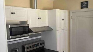 A compact kitchen with white cabinets, a microwave, a stove, and a coffee maker.