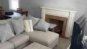 A living room with a sectional sofa, a fireplace, a television, and a dining area in the background.
