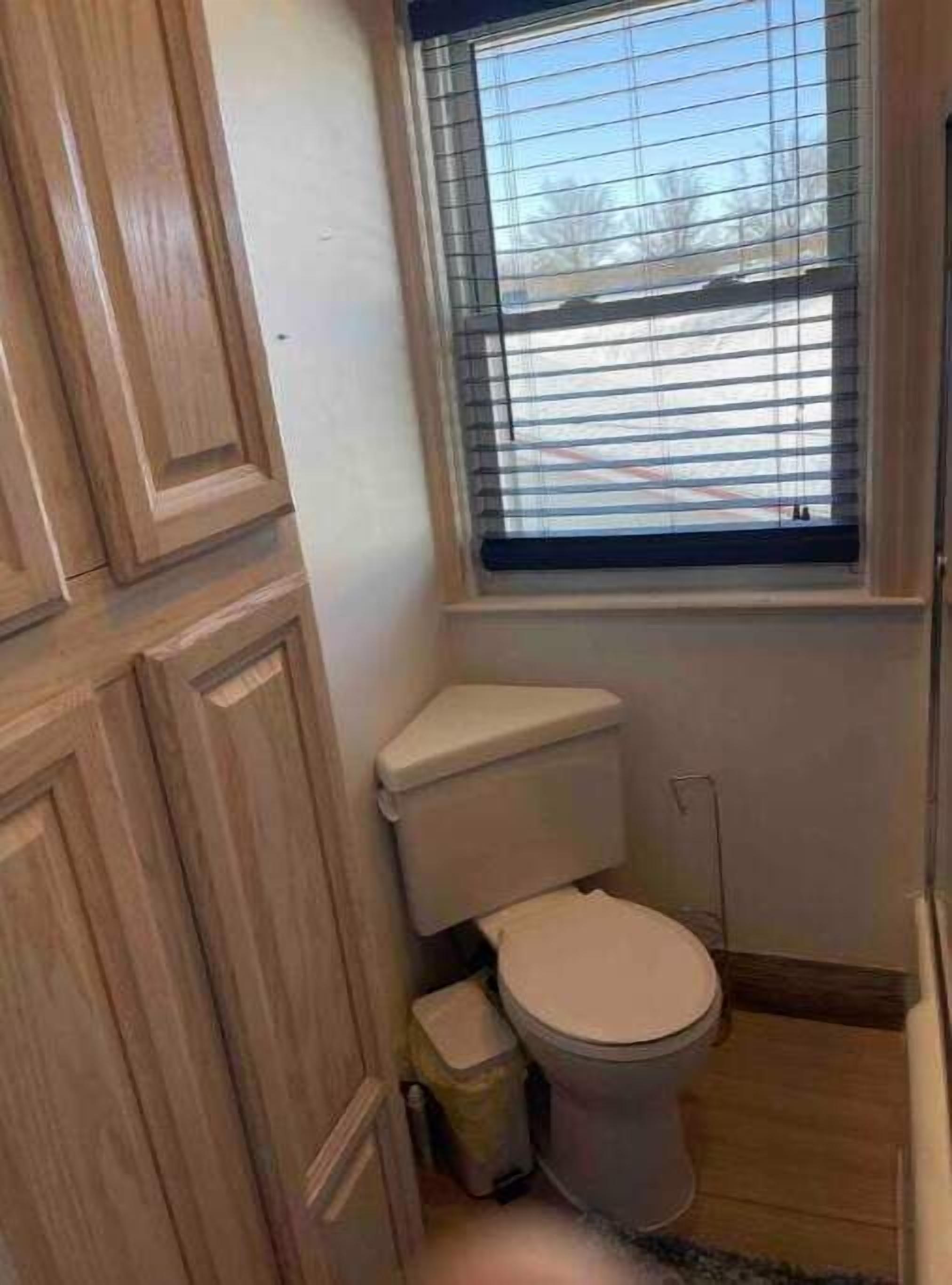 A small bathroom with a toilet, a wooden cabinet, and a window with blinds.