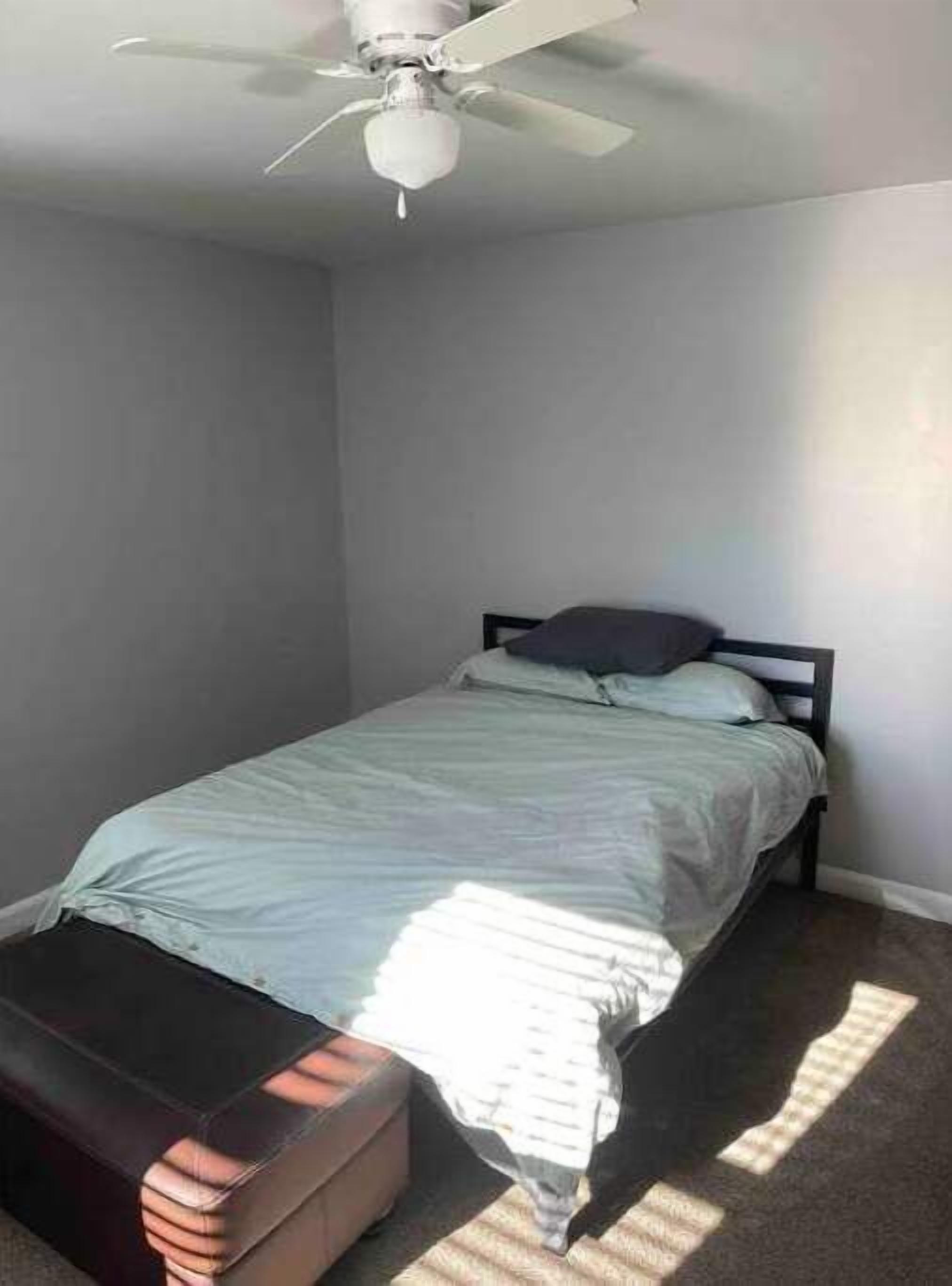 A bedroom with a single bed, a ceiling fan, and a suitcase on the floor.