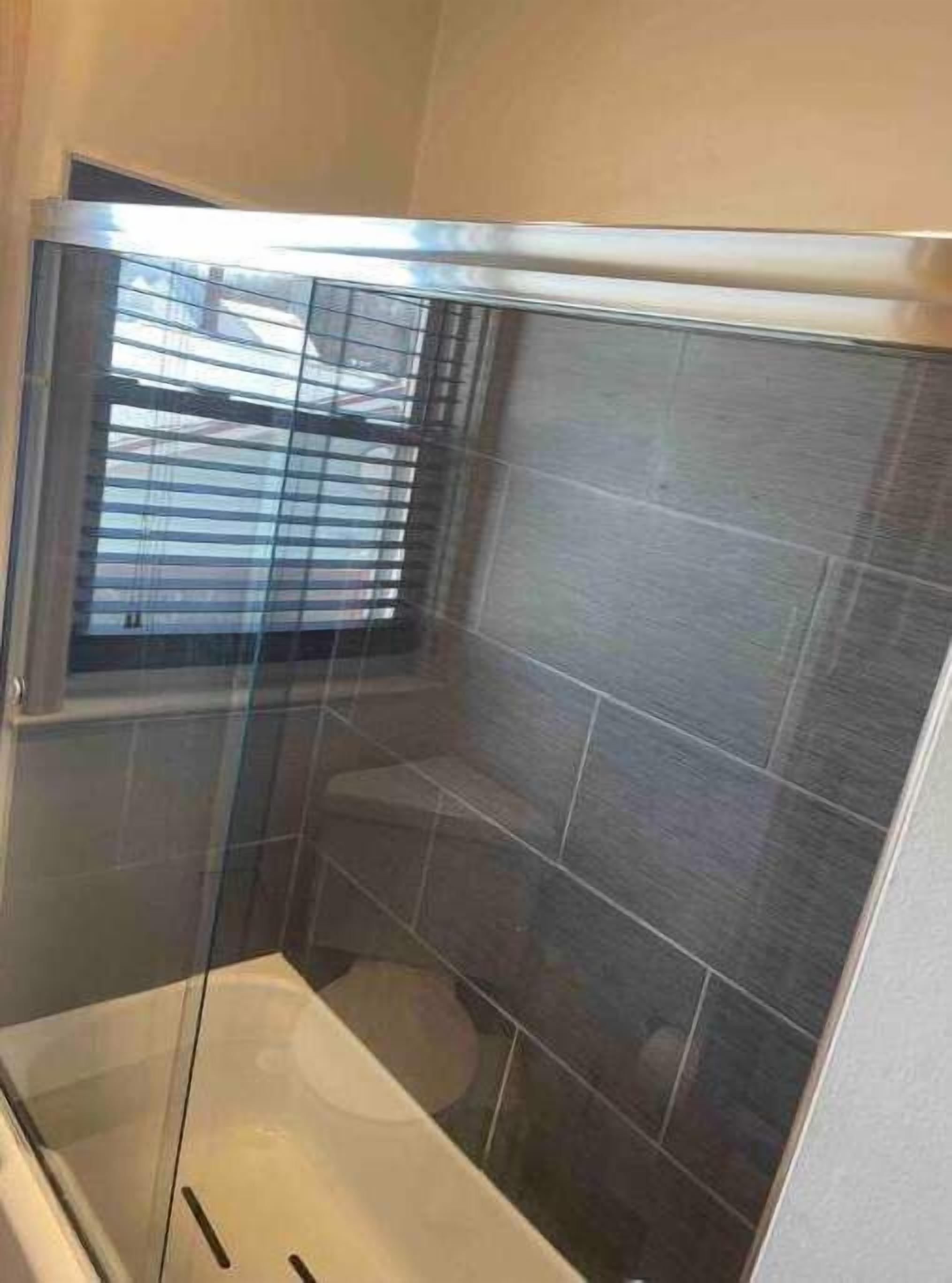 Een kleine, afgesloten douchecel met een glazen deur, betegelde wanden en een zichtbaar toilet.