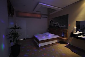 A modern bedroom with a bed, a wall-mounted artwork, a bedside table, and a potted plant. - PRIME MOTEL  (Campinas)