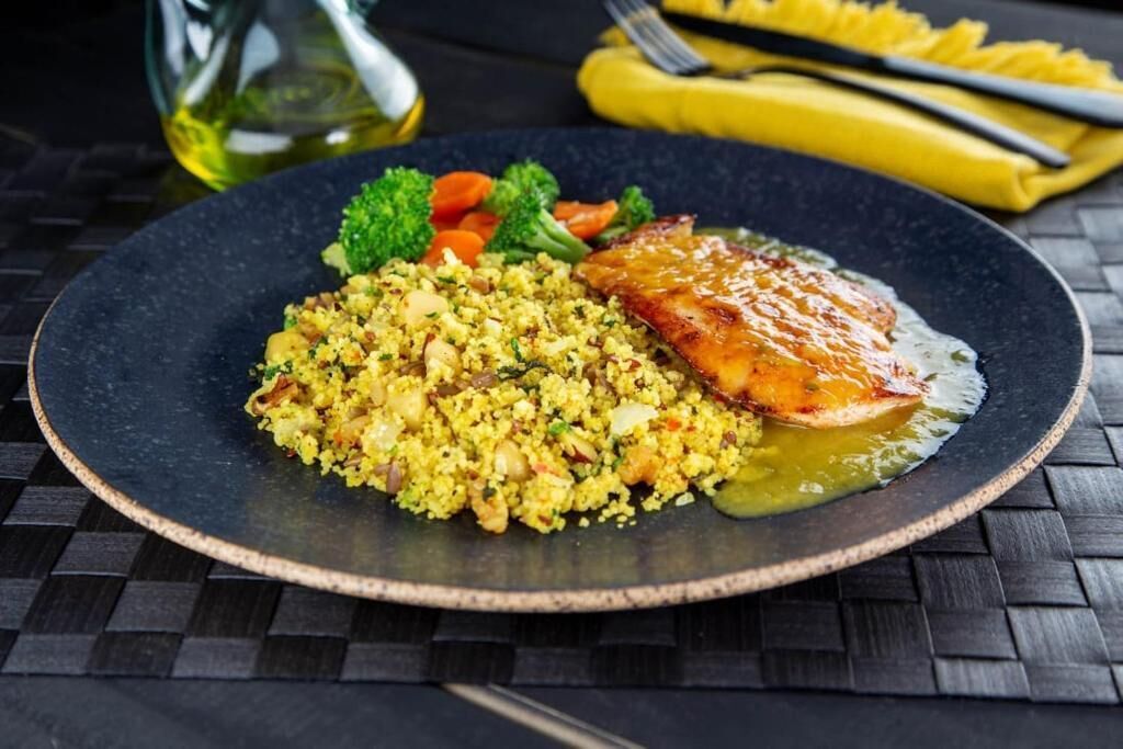 Um prato com um pedaço de carne grelhada e um acompanhamento de cuscuz.