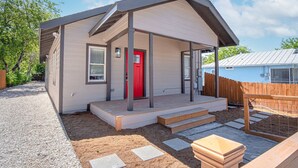A single-story house with a red door, a covered porch, and a fenced backyard. - Delightfully Renovated 4 BR 2 BA Near DT Riverwalk (San Antonio)