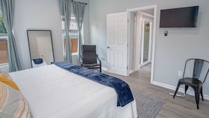 A bedroom with a bed, a chair, a TV, and a door leading to another room. - Delightfully Renovated 4 BR 2 BA Near DT Riverwalk (San Antonio)