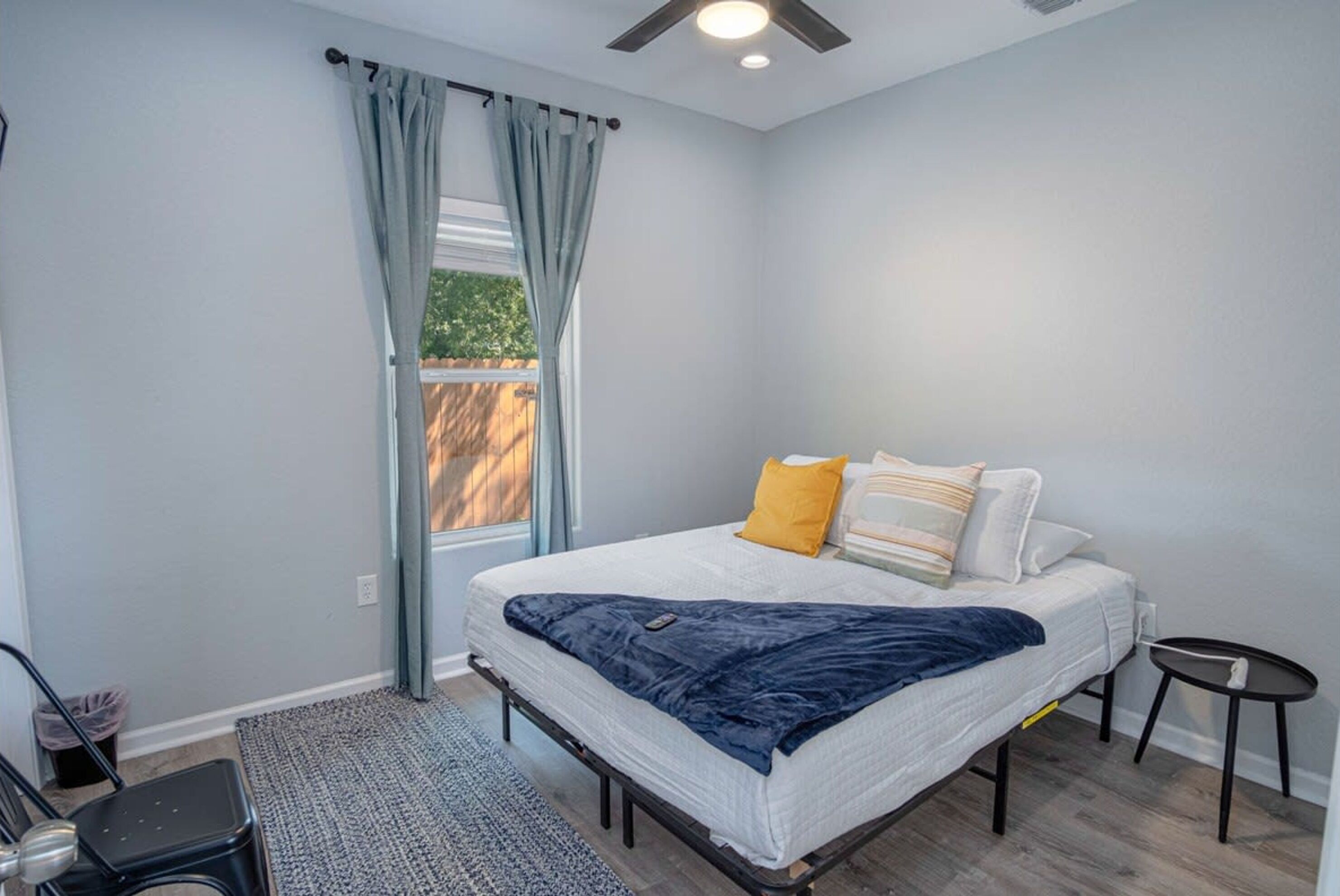 A bedroom with a bed, a small table, a chair, and a window with curtains.