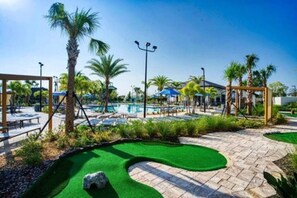 A pool area with palm trees, lounge chairs, and a small putting green.