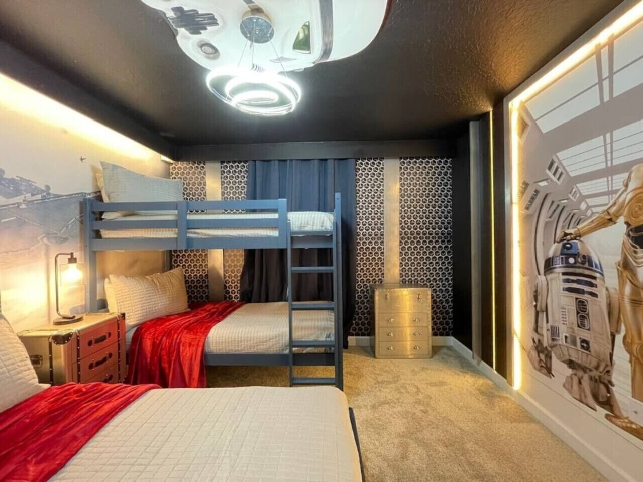 A bunk bed room with a ladder, a dresser, a wall-mounted lamp, and a poster of a space-themed character.