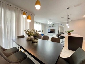 A modern dining area with a long table, chairs, pendant lights, and a vase with flowers.