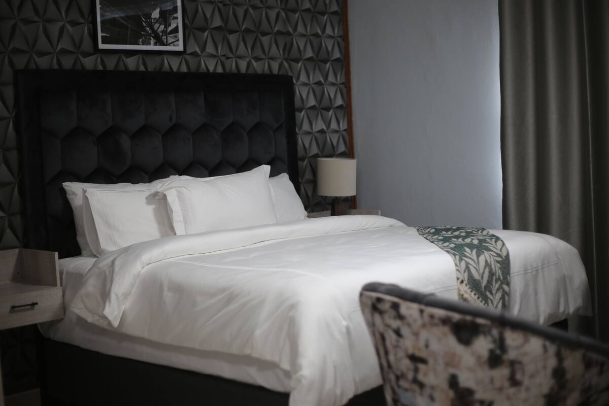 A neatly made bed with white linens, a dark headboard, and a patterned throw blanket.