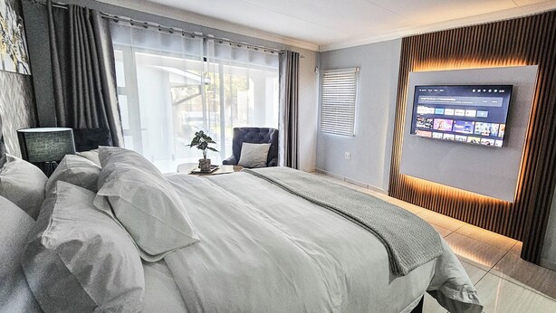A modern hotel room with a large bed, a TV mounted on the wall, and a window with curtains.