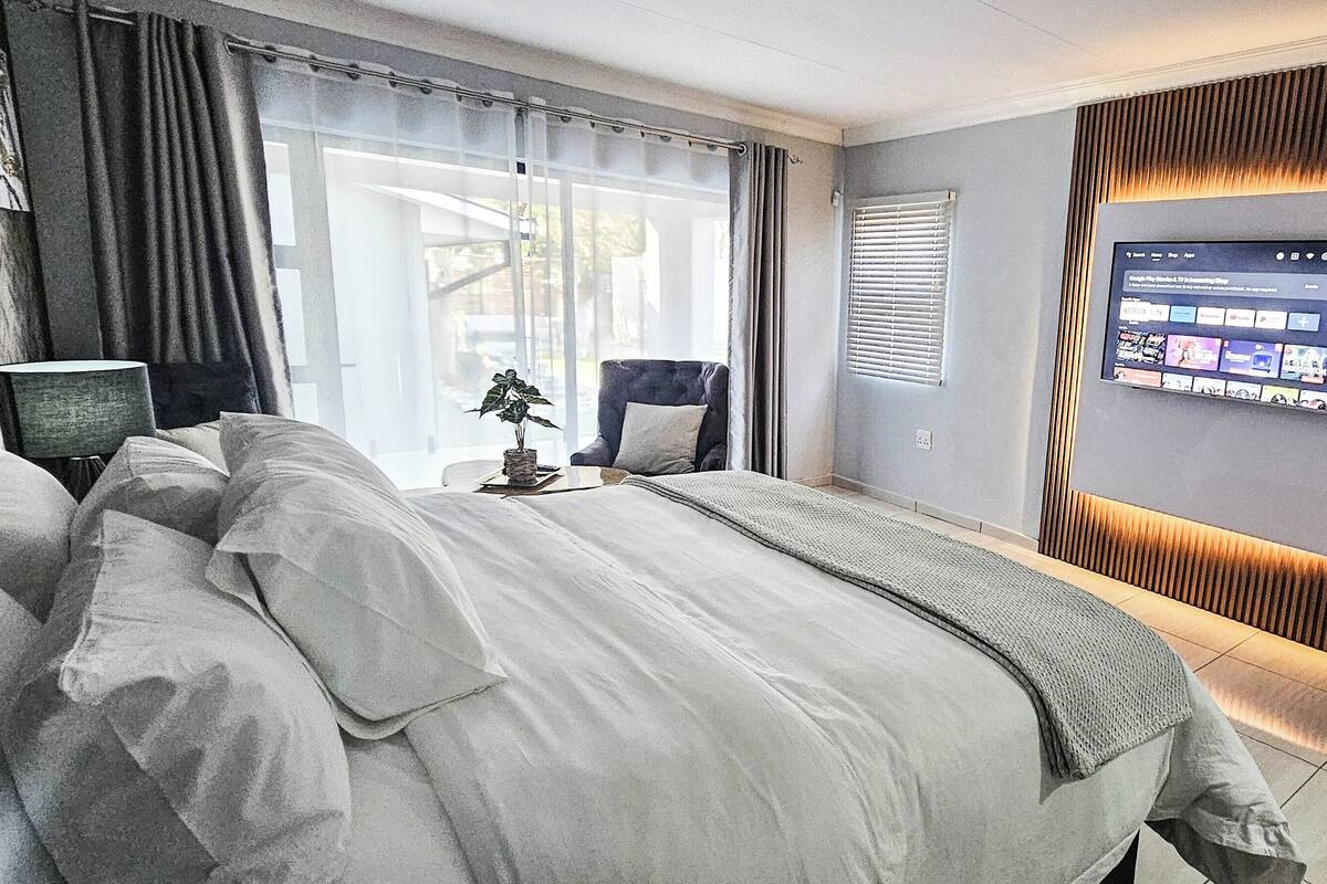 A modern hotel room with a large bed, a TV mounted on the wall, and a window with curtains.